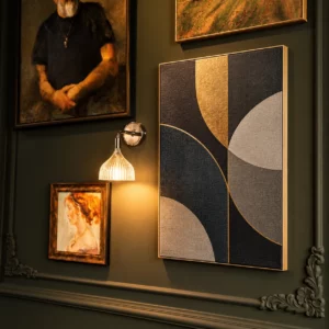 Textilspannrahmen mit geometrischem Motiv in Schwarz, Grau und Gold und schmalem Goldprofil an einer dunkelgrünen Wand neben gerahmten Gemälden
